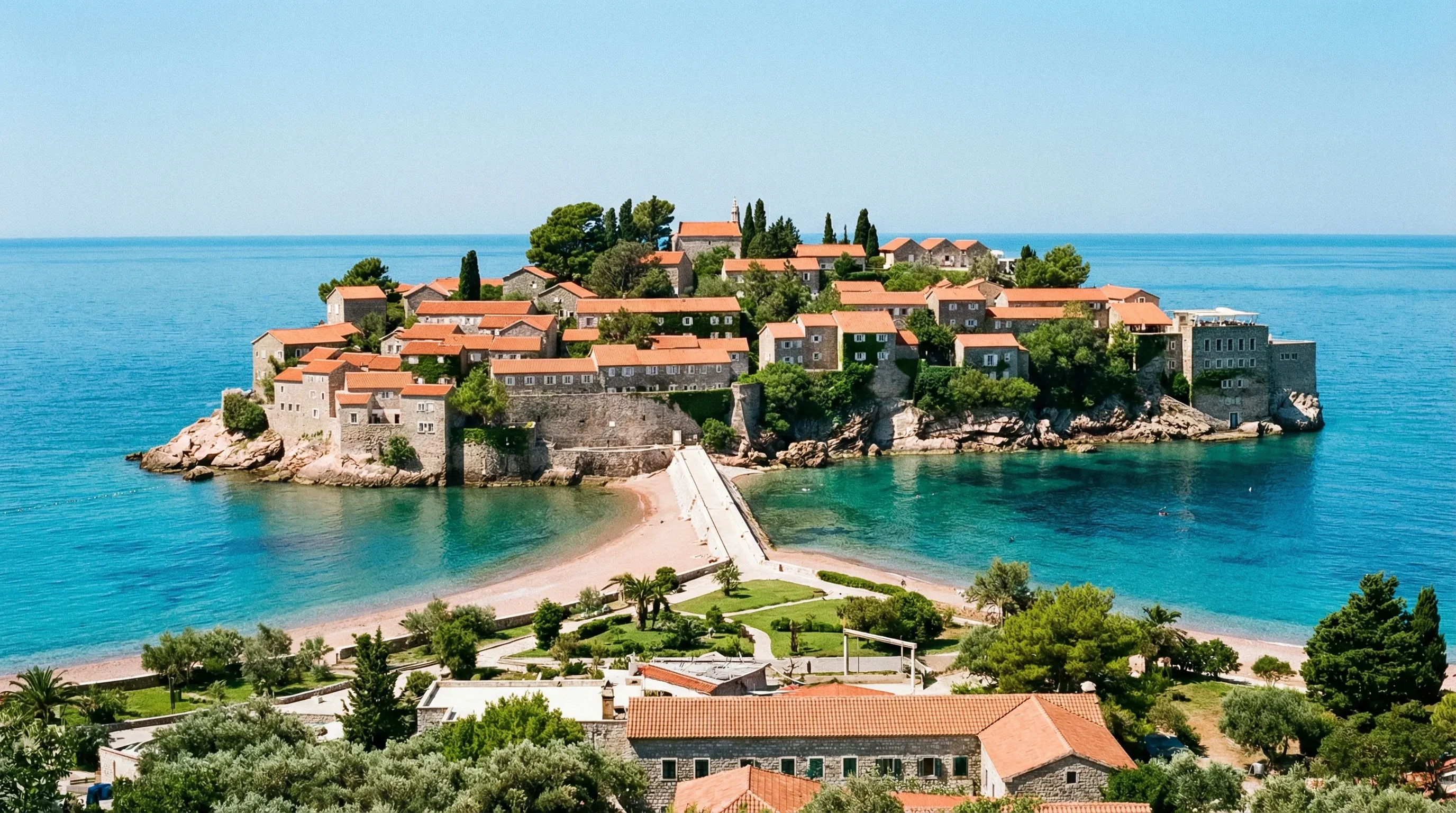 The fortified island-hotel of Sveti Stefan, featuring red-tiled roofs and stone walls, connected to the mainland by a narrow causeway in the Adriatic Sea.