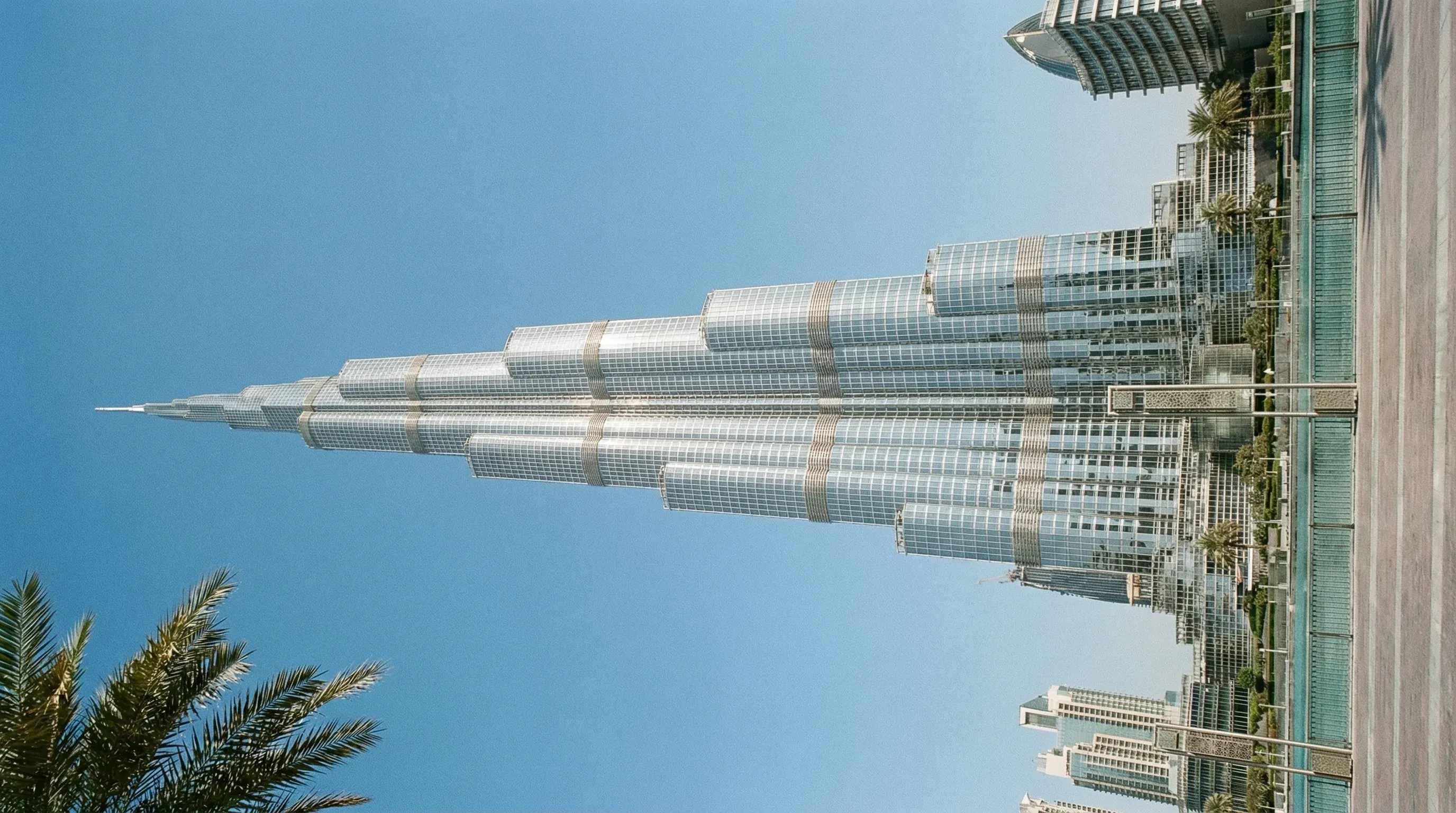The Burj Khalifa skyscraper stands against a bright blue sky above the modern buildings of Downtown Dubai.