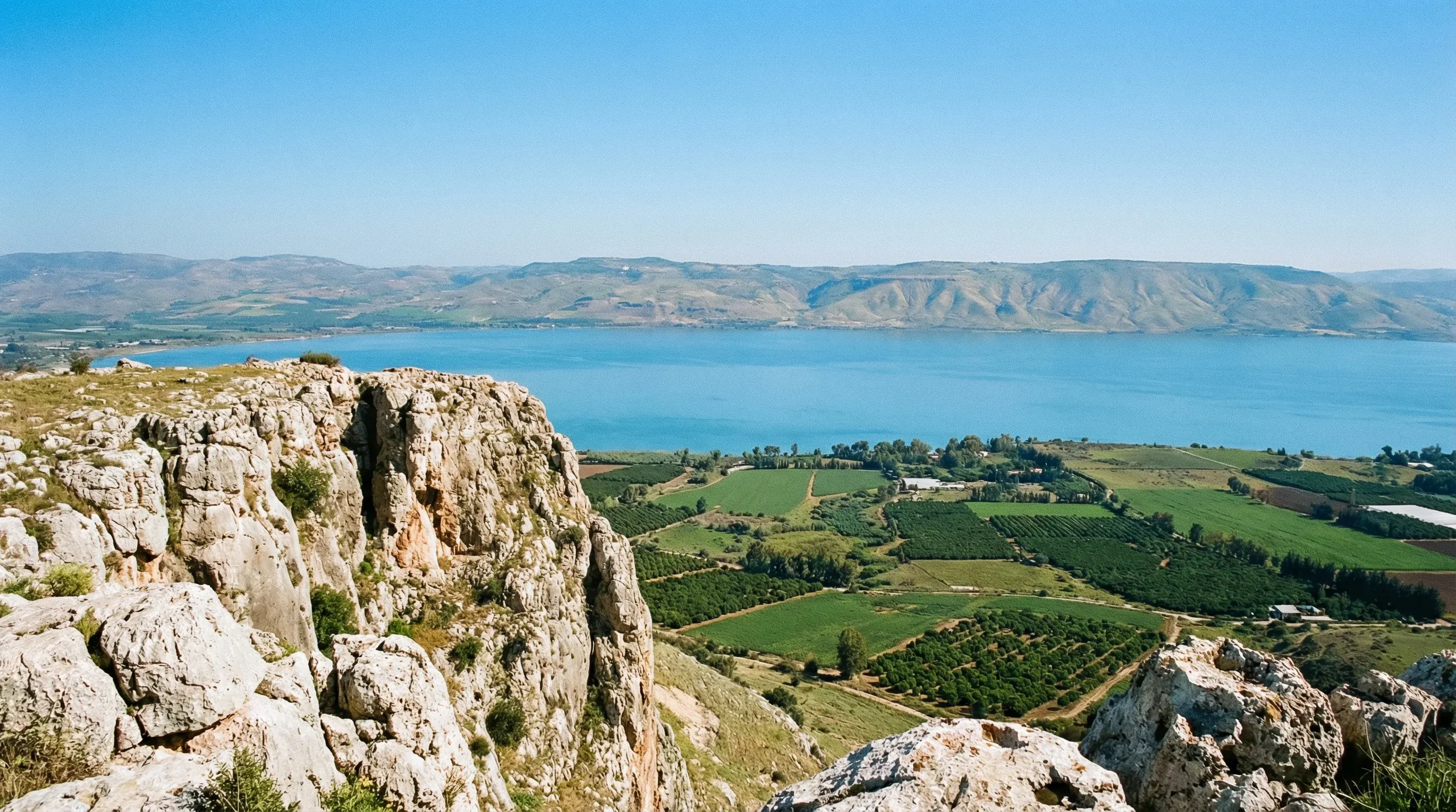 A panoramic view from the rocky cliffs of Mount Arbel looking down at the blue Sea of Galilee and green valleys.