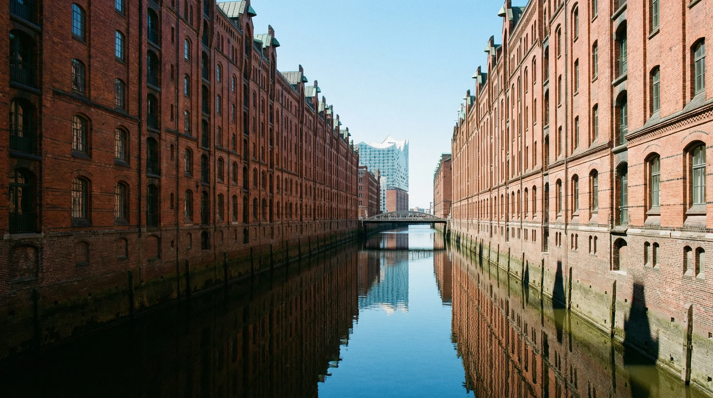 Red brick warehouses line a canal in Hamburg's Speicherstadt district with the Elbphilharmonie in the distance.
