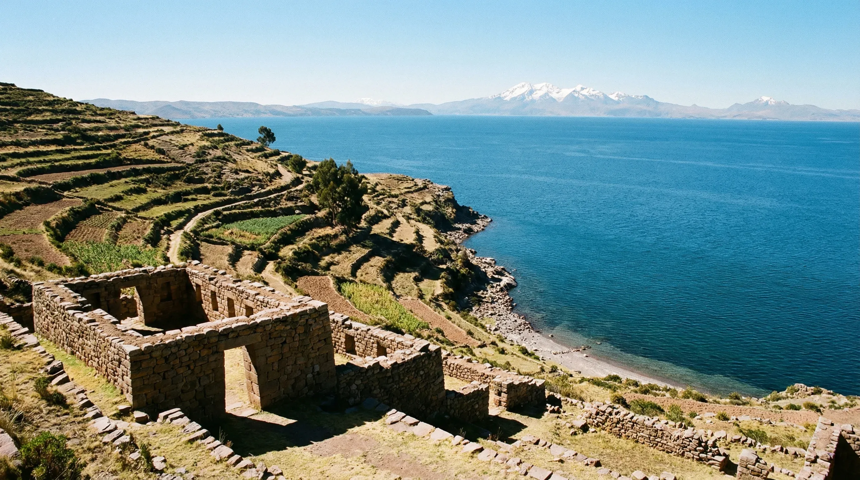 Ancient stone ruins on a terraced island overlooking a large blue lake with snow-capped mountains in the distance.