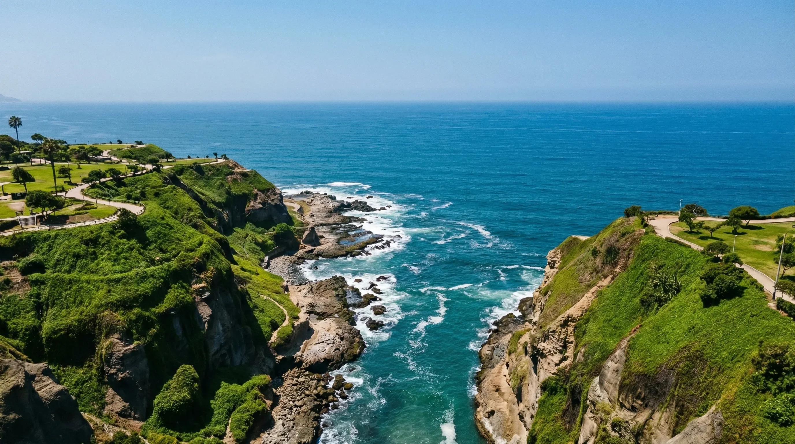 The steep green cliffs of the Lima coastline meeting the Pacific Ocean on a clear, sunny day.