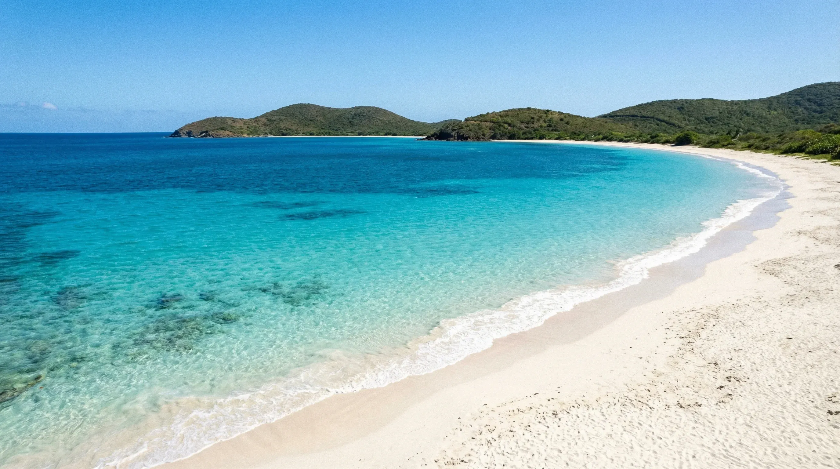 A wide white sand beach with turquoise water and green hills on Culebra Island.