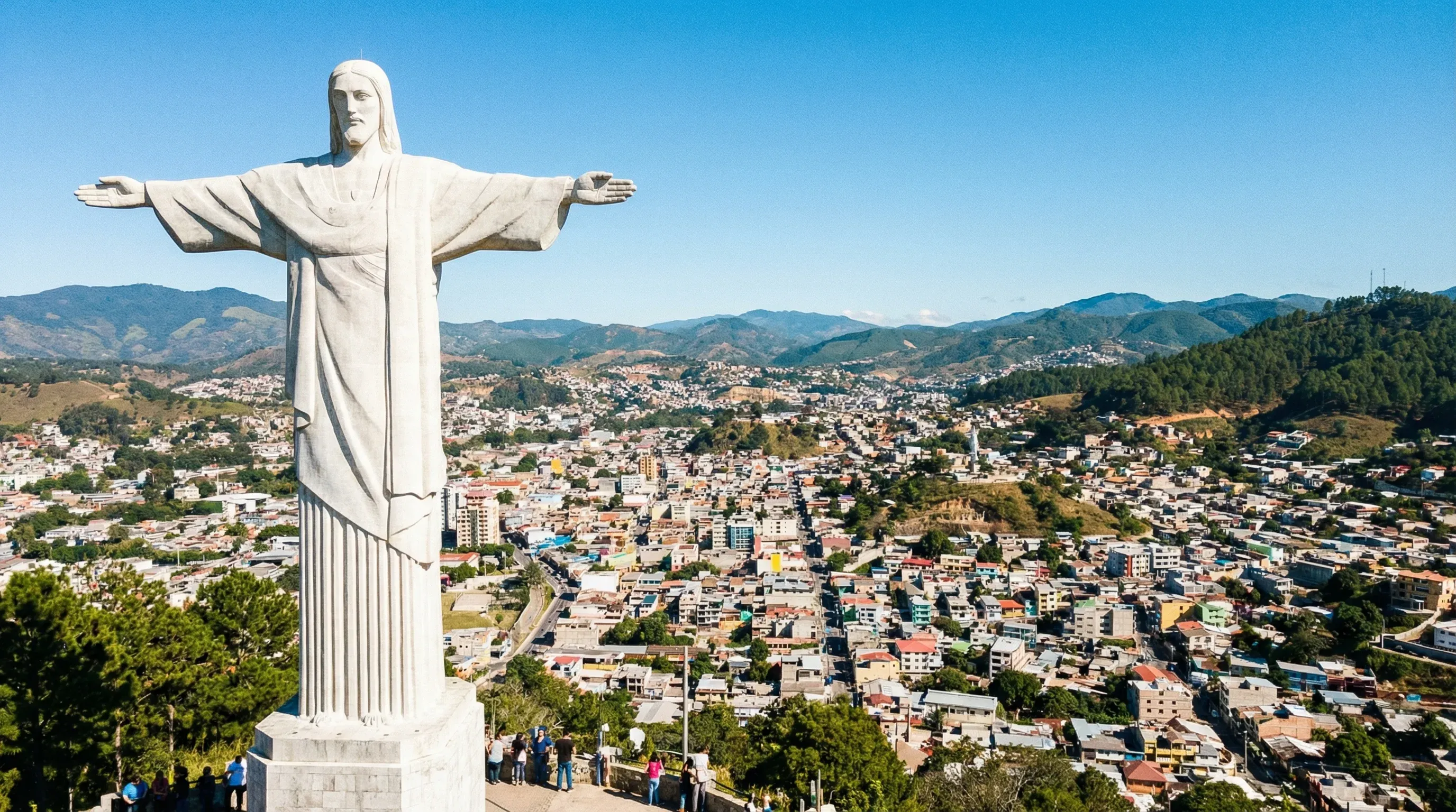 The white stone Christ of the Picacho statue overlooks the sprawling valley city of Tegucigalpa under a bright sky.