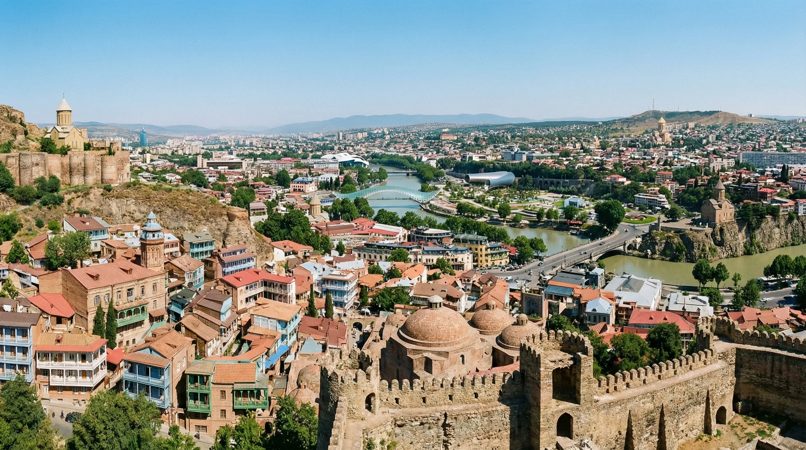 A panoramic view of Old Tbilisi showing Narikala Fortress, traditional houses with colorful balconies, and the Mtkvari River.