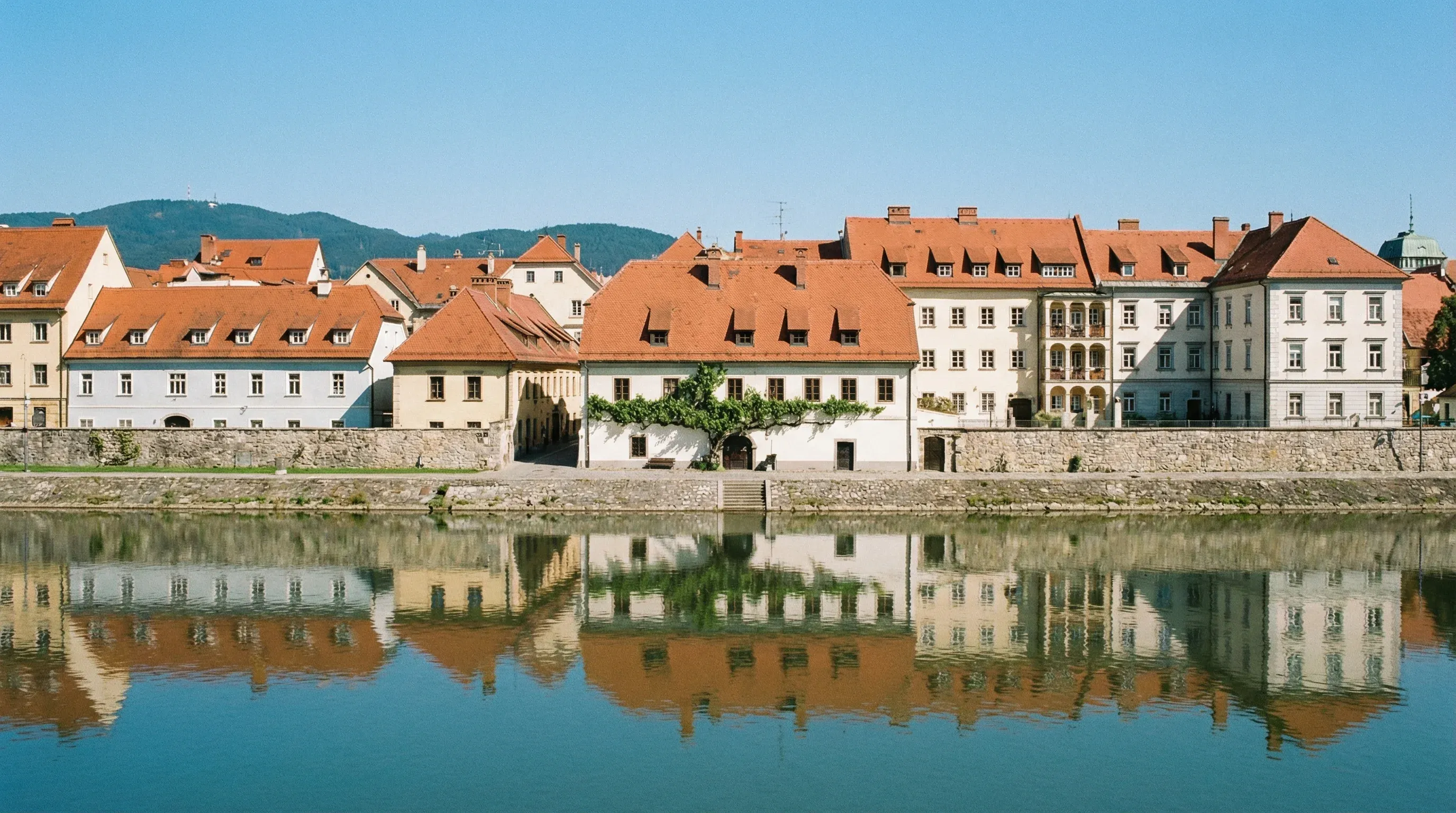 The Lent district in Maribor showing the historic Old Vine House and red-roofed buildings along the Drava River.