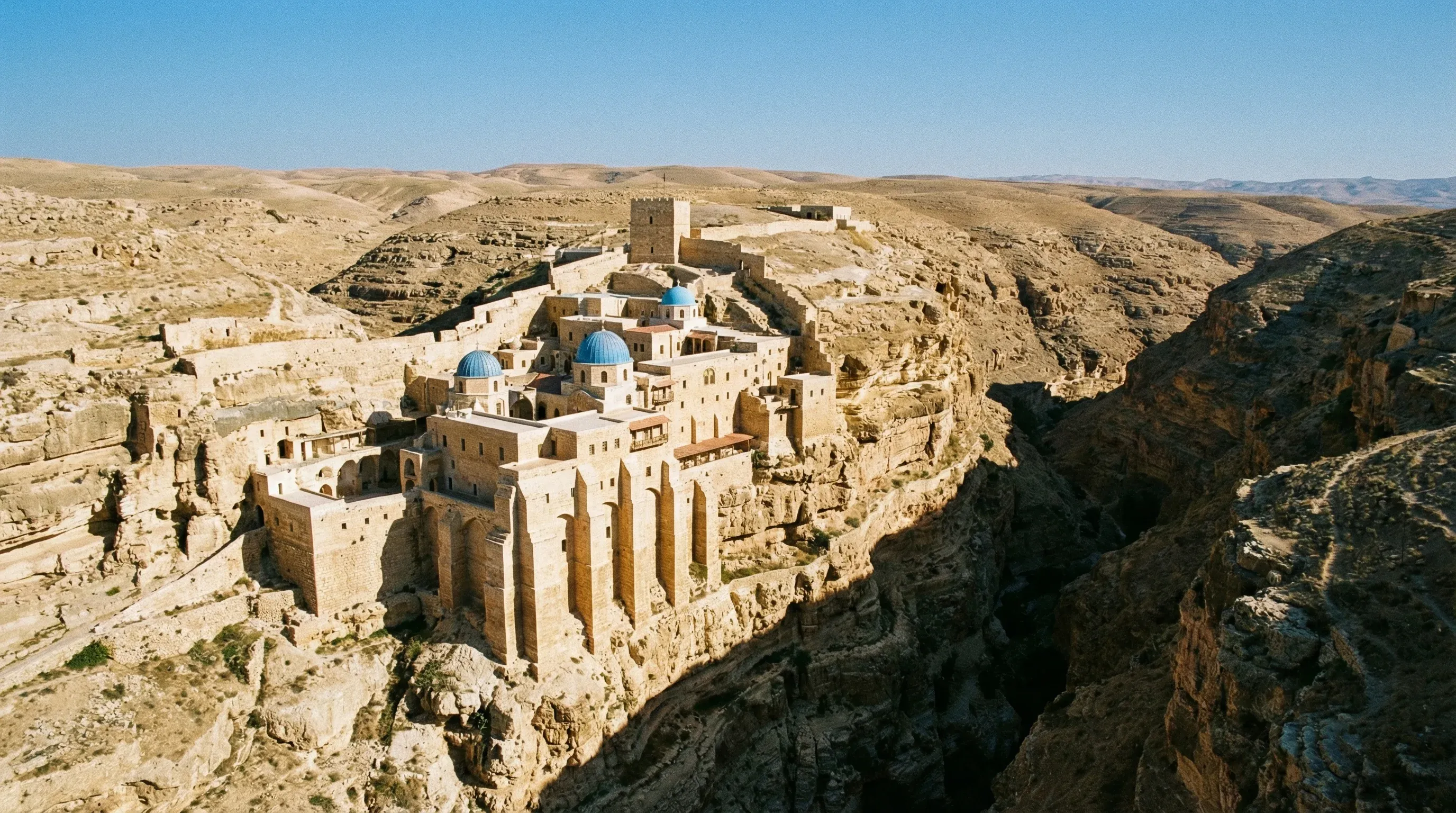 The ancient Mar Saba Monastery built into the side of a steep desert canyon in the Judean Wilderness under a clear sky.