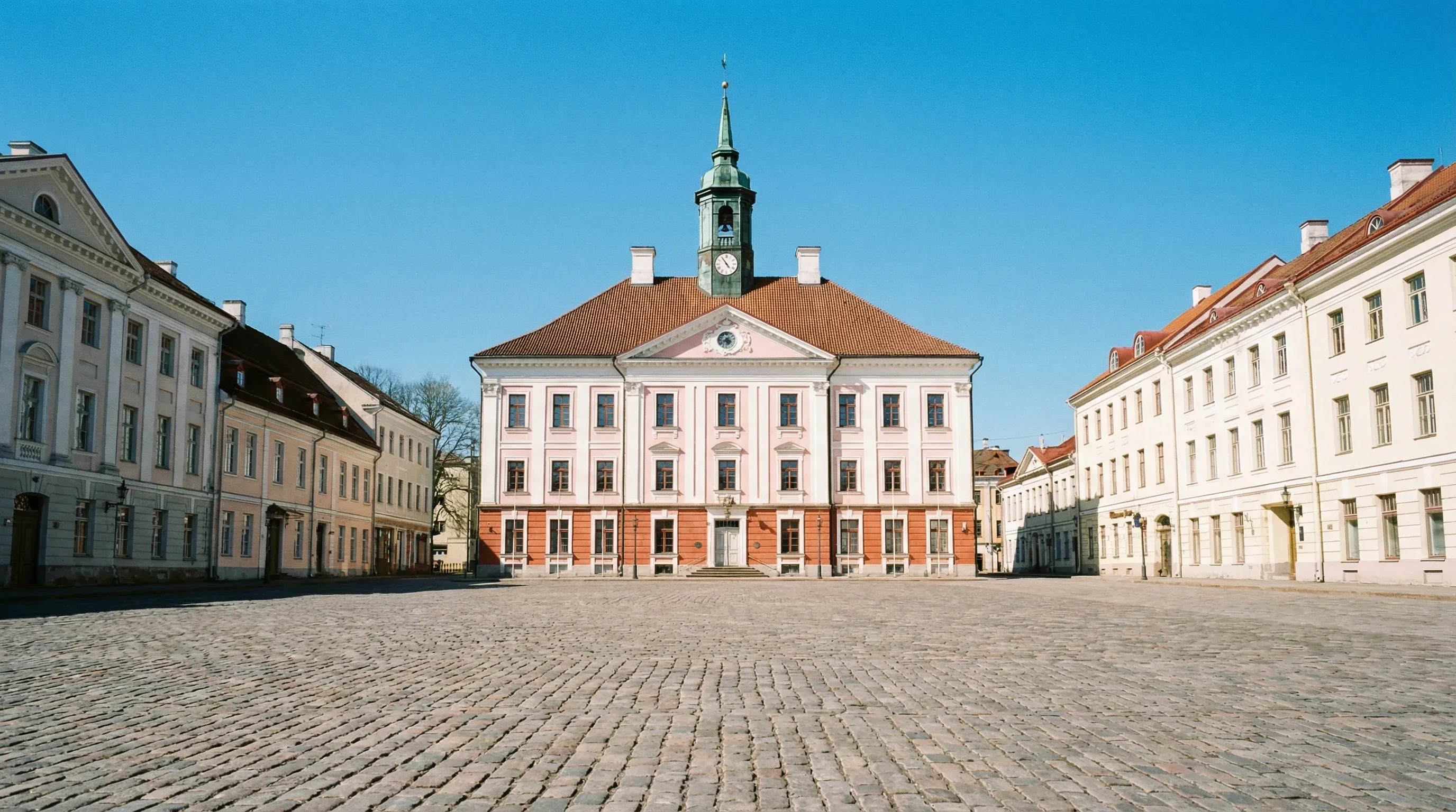 The neoclassical pink and white Town Hall of Tartu standing in a cobblestone square.