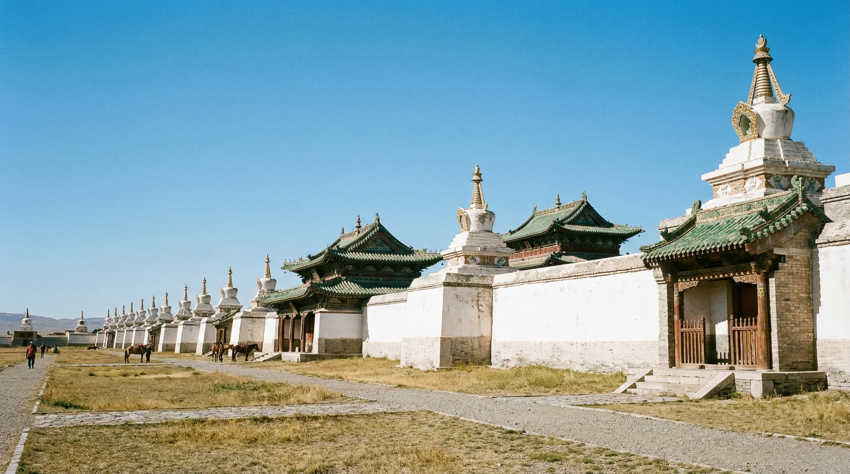 The white stupa-lined walls and traditional temples of Erdene Zuu Monastery in Kharkhorin, Mongolia, under a clear blue sky.