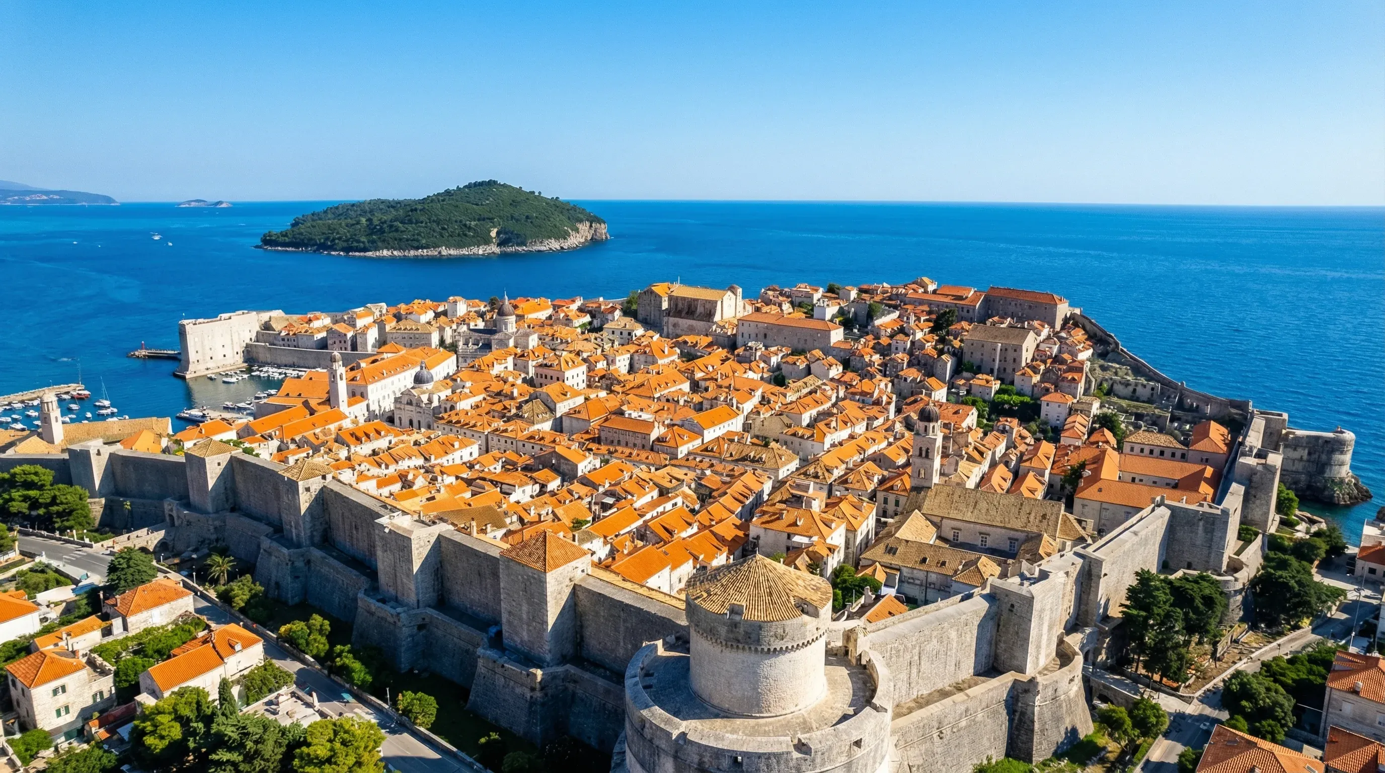 A panoramic elevated view of the historic walled city of Dubrovnik and its red-roofed buildings by the sea.