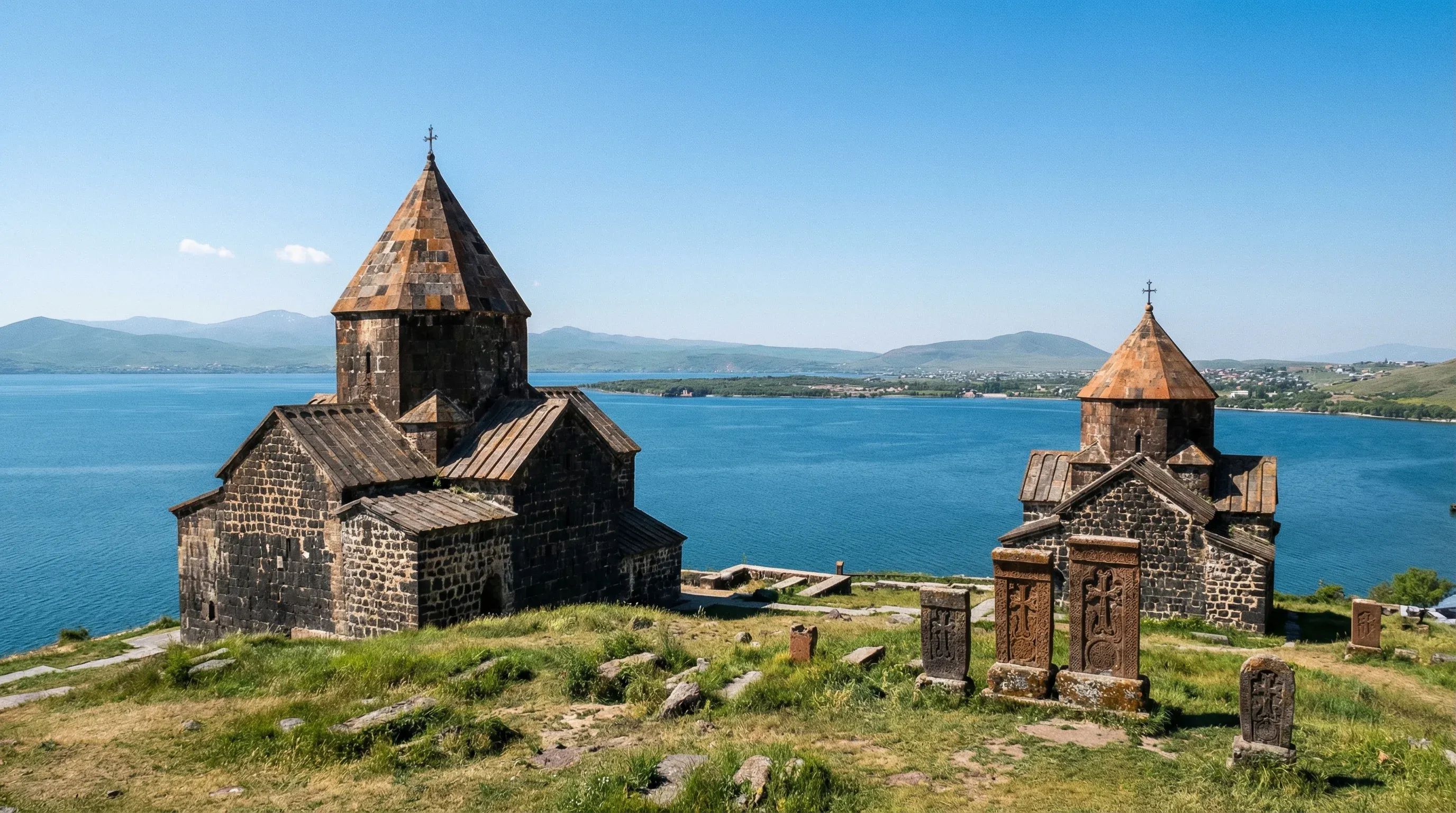 The ancient dark stone churches of Sevanavank Monastery overlook the deep blue waters of Lake Sevan under a clear sky.
