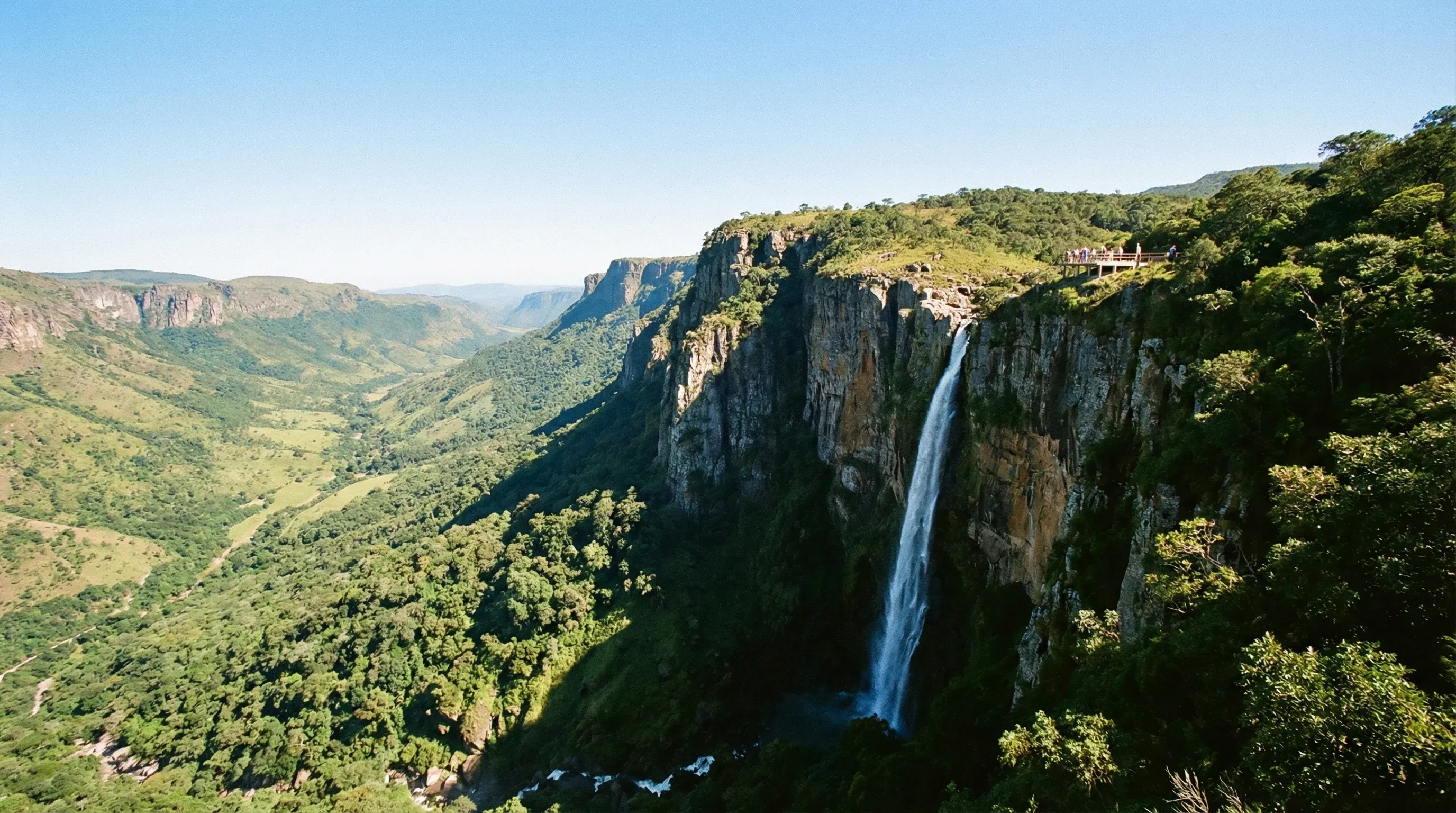 A high-angle view of Mutarazi Falls dropping into a green valley under a clear blue sky in Zimbabwe's Eastern Highlands.