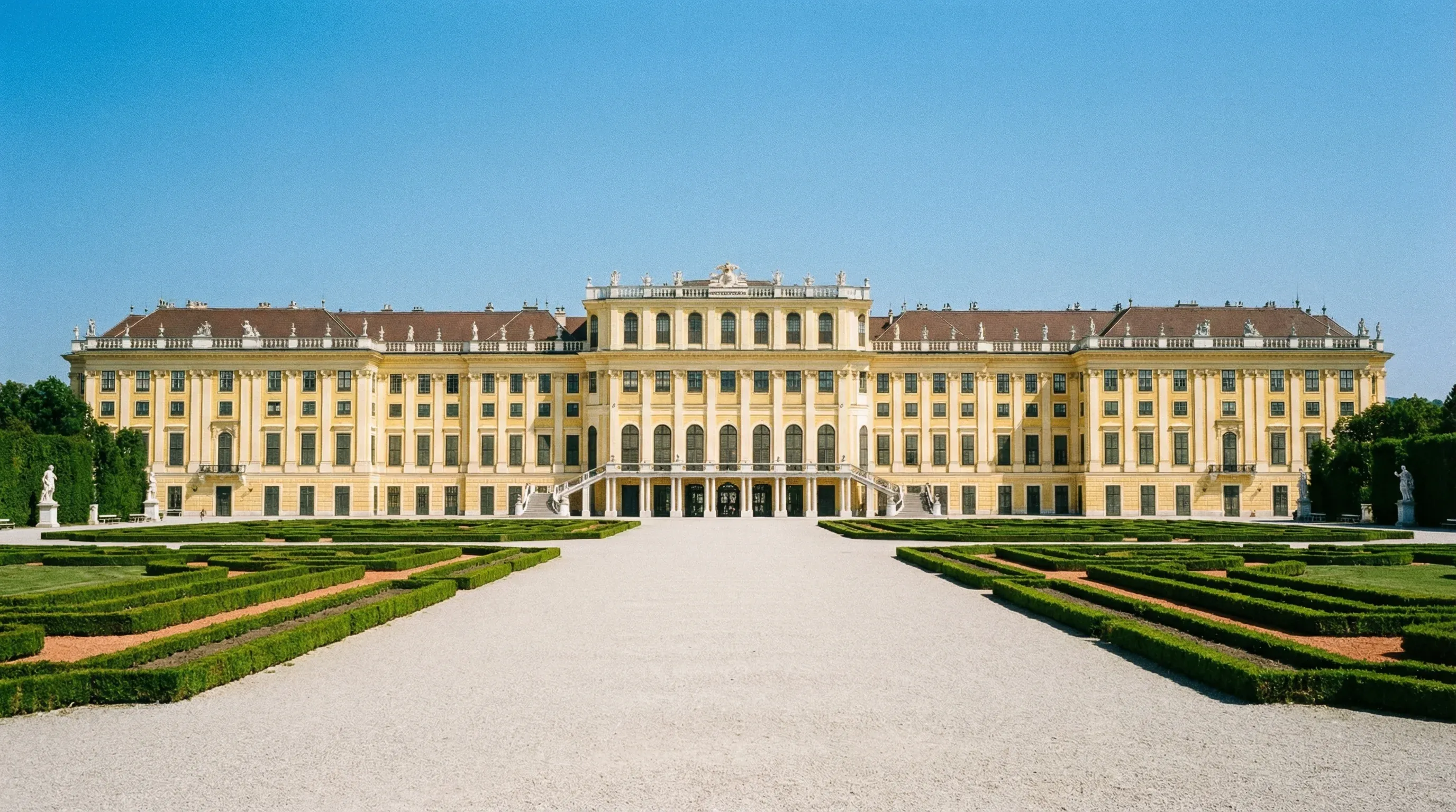 The yellow façade of Schönbrunn Palace and its symmetrical formal gardens under a bright, clear sky.