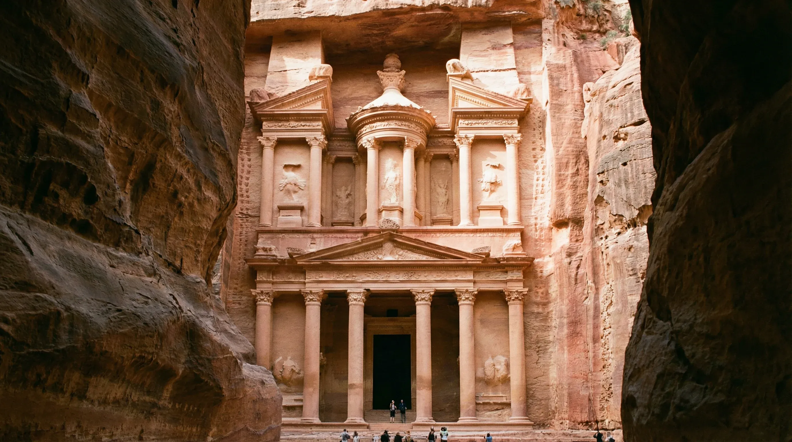 A view from the Siq canyon opening toward the Treasury at Petra, showing the detailed rock-cut architecture of the rose-red city.