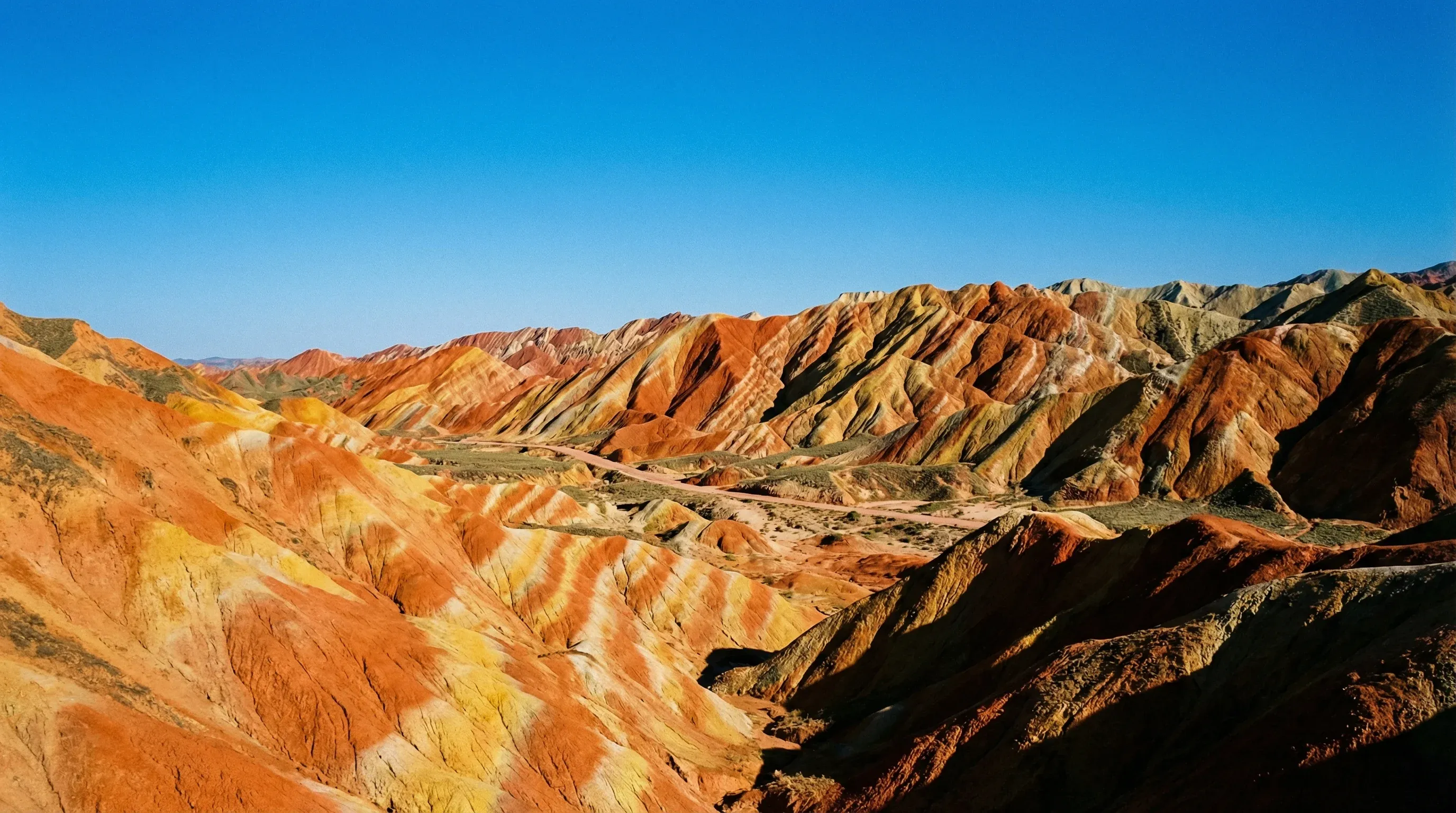 Colorful, striped sandstone hills in shades of red and orange under a clear blue sky in Zhangye.
