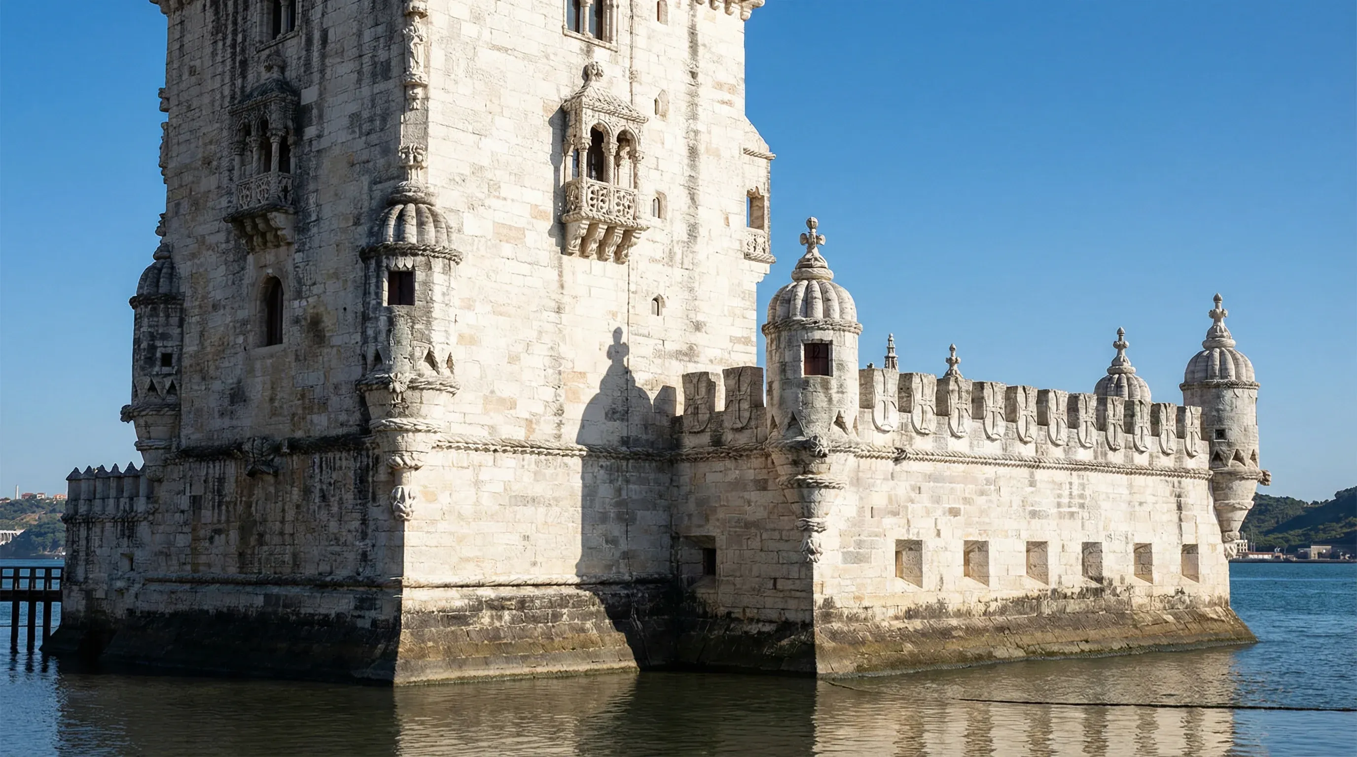 The historic Belém Tower made of white stone on the edge of the Tagus River in Lisbon during a sunny day.