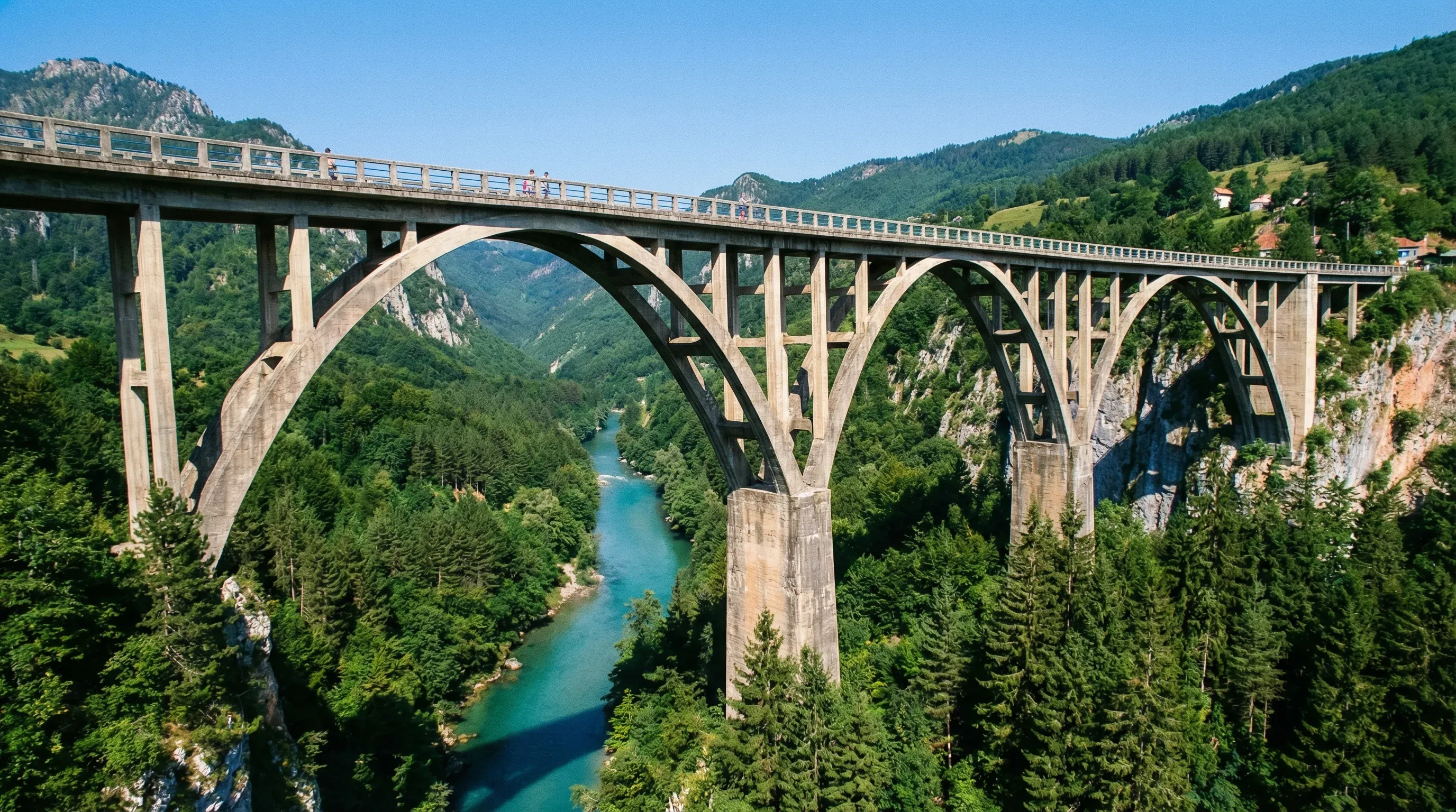 The large concrete arches of the Đurđevića Tara Bridge spanning a deep green river canyon surrounded by dense evergreen forests.