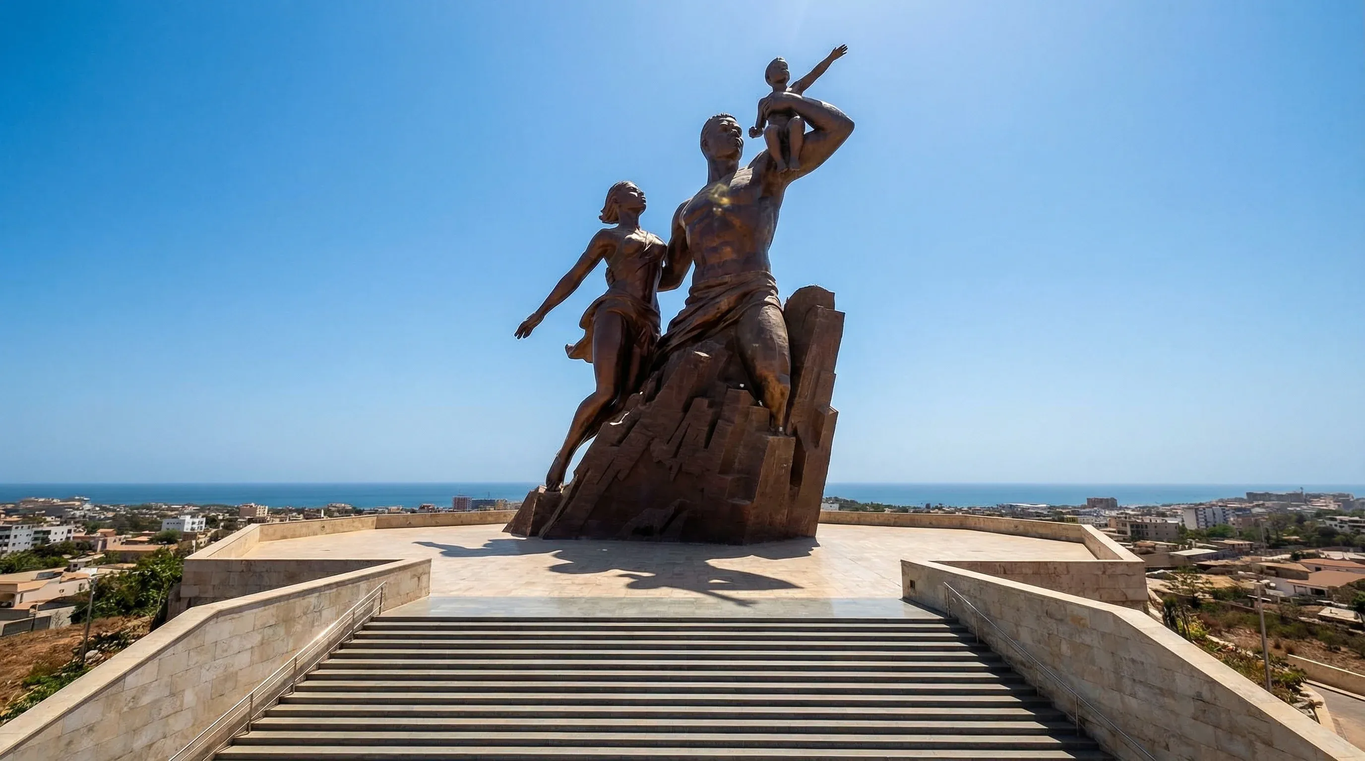 The massive bronze African Renaissance Monument standing on a hilltop in Dakar, Senegal, against a clear sky.