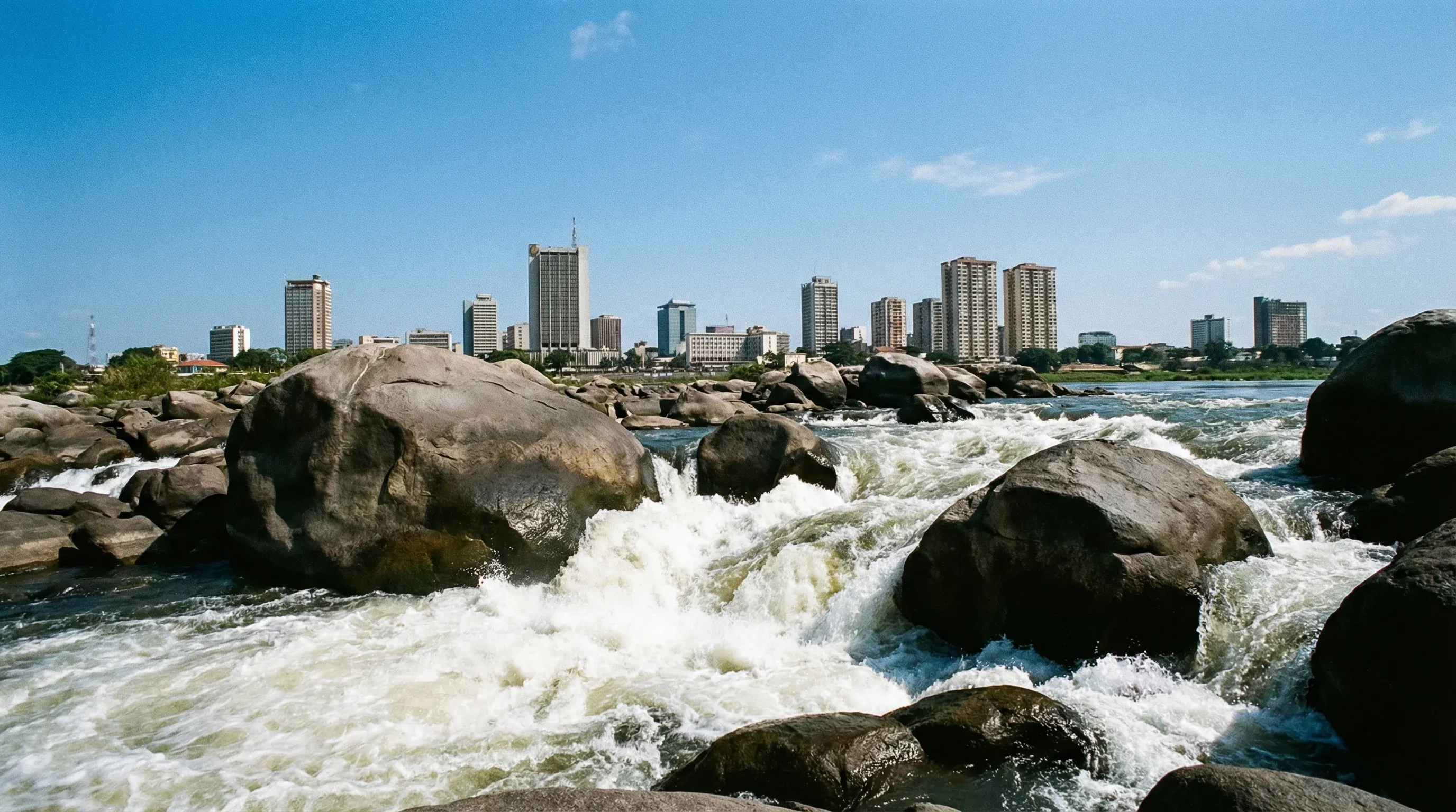 White water rapids on the Congo River in the foreground with the Kinshasa city skyline in the distance.
