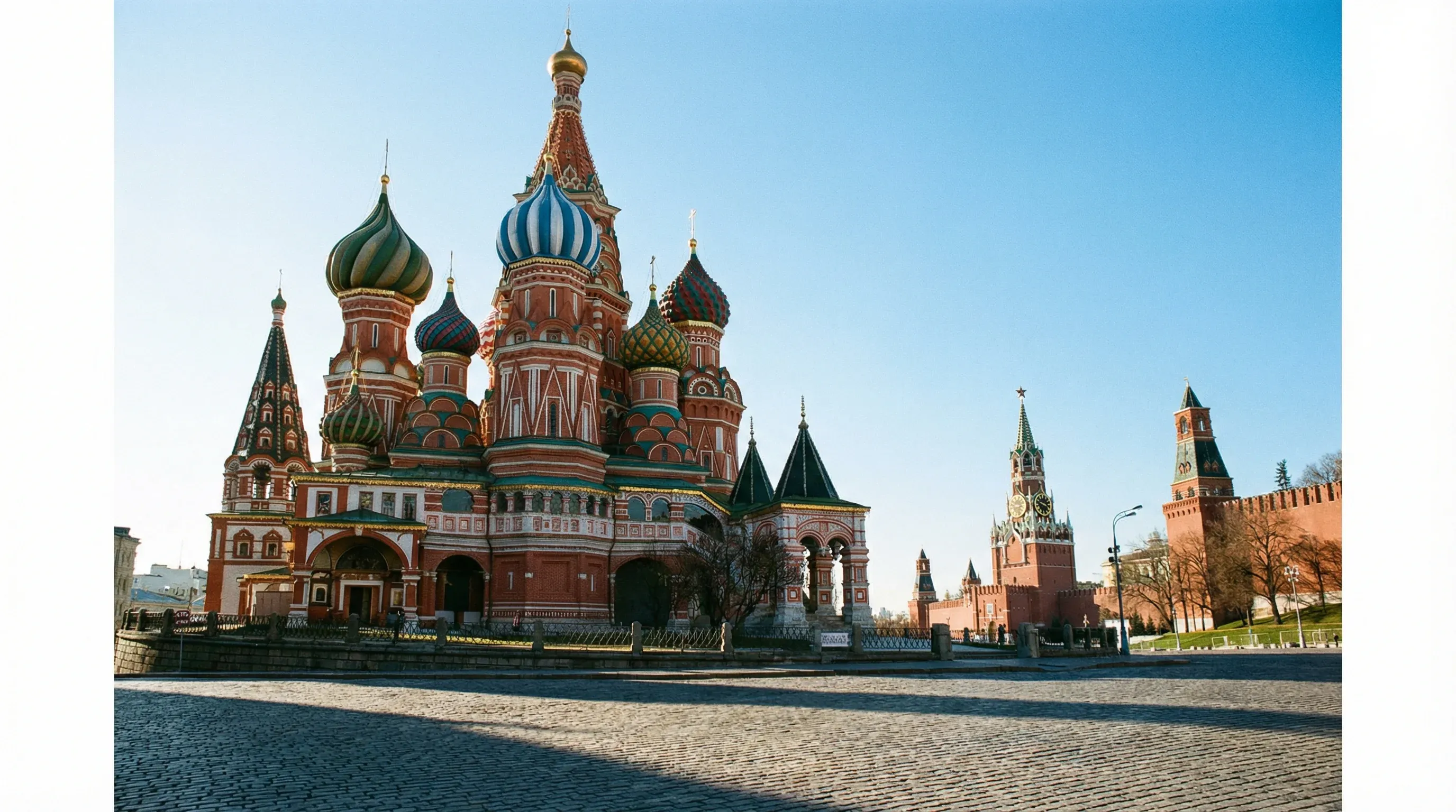A wide view of Saint Basil's Cathedral in Red Square, Moscow, showing its multi-colored onion domes under a clear blue sky.