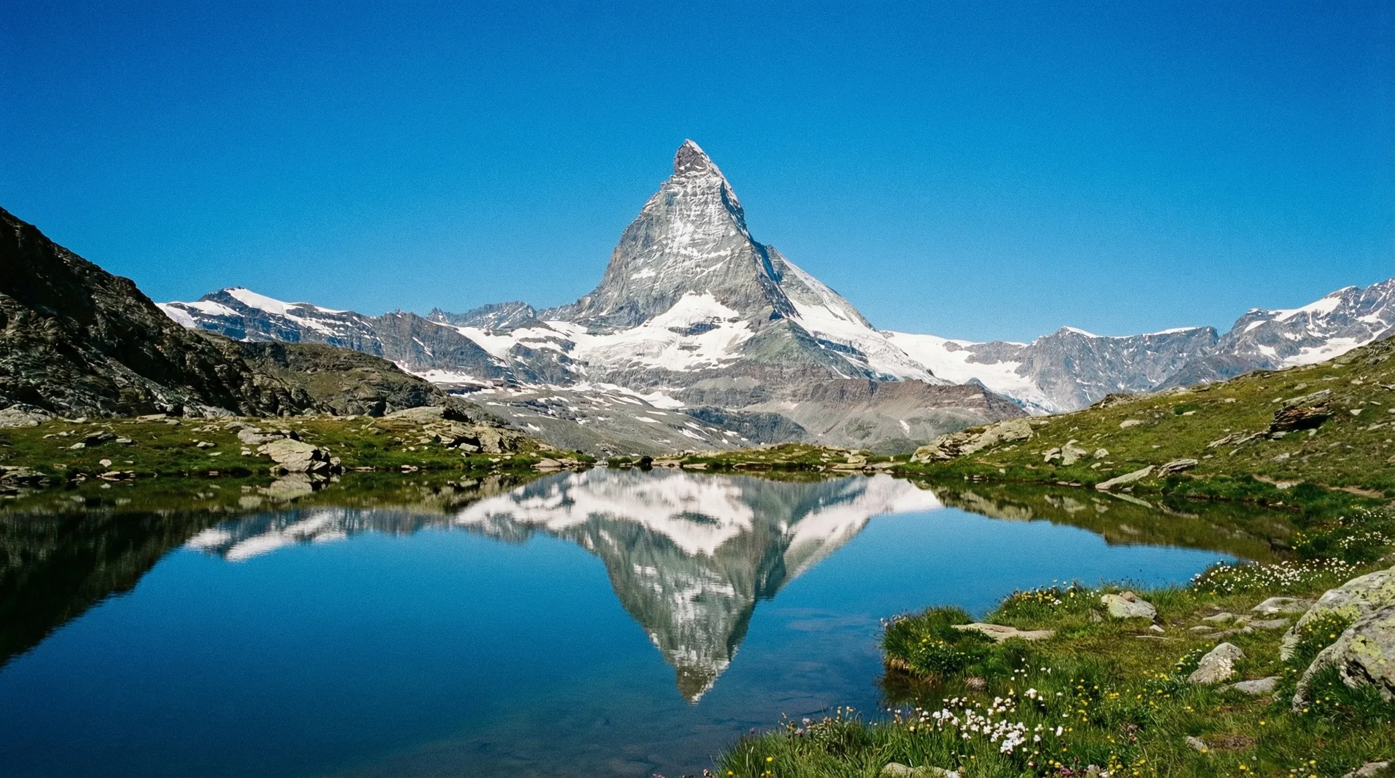 The iconic pyramid-shaped Matterhorn mountain peak reflecting in a small alpine lake under a clear sky.