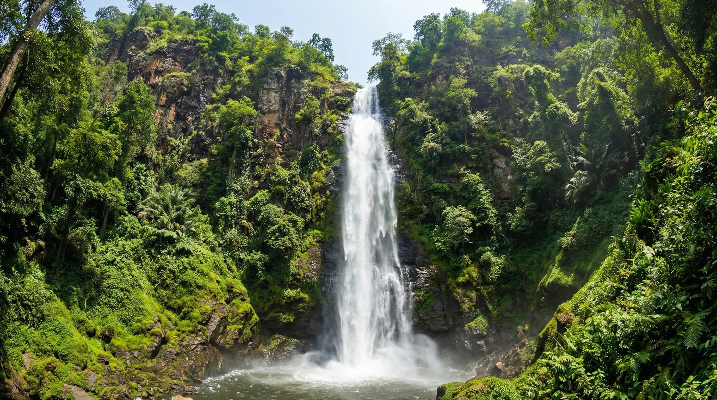 The high Wli Waterfalls cascading down a rocky cliff surrounded by dense green tropical forest.