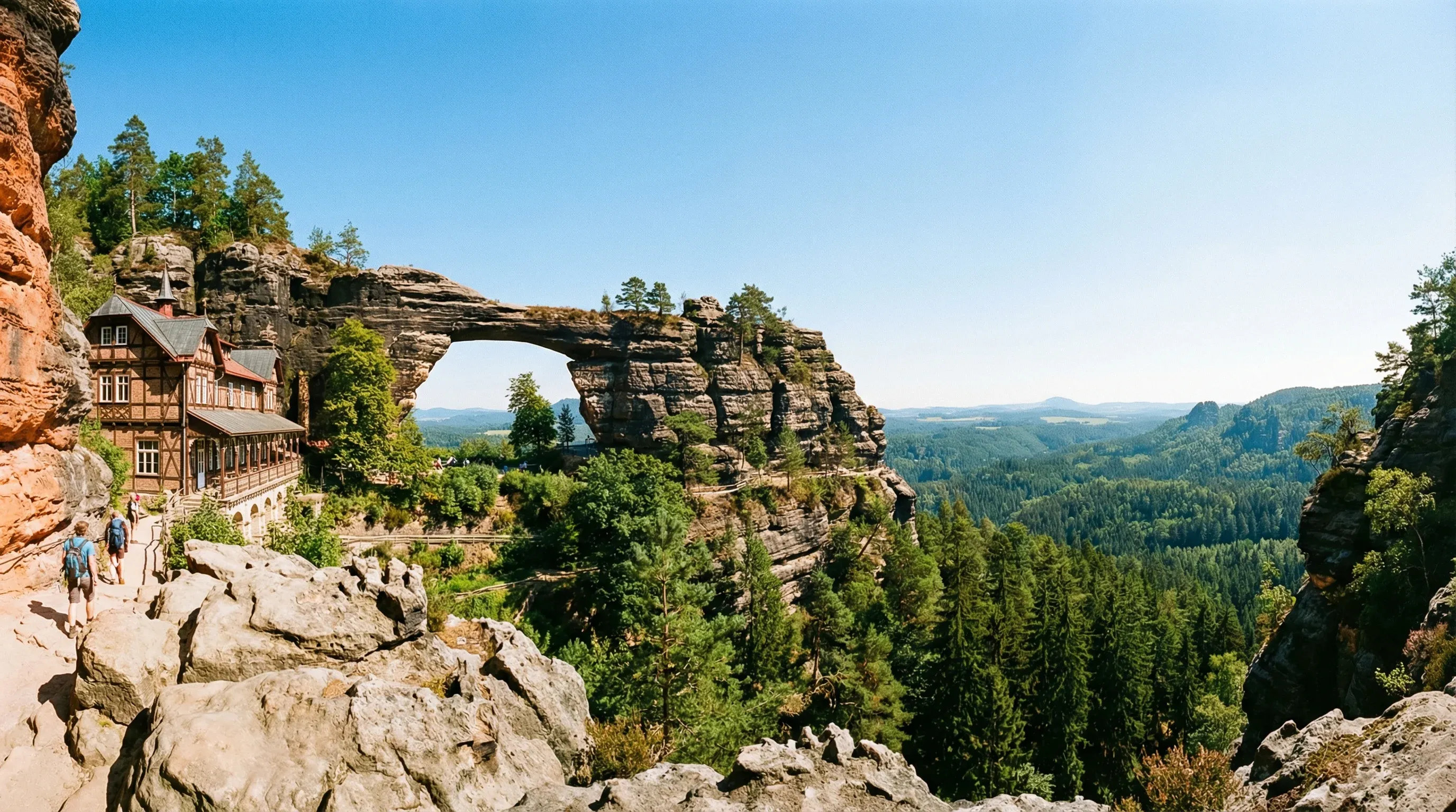 The massive natural sandstone arch of Pravčická brána beside the historic Falcon's Nest building in North Bohemia.