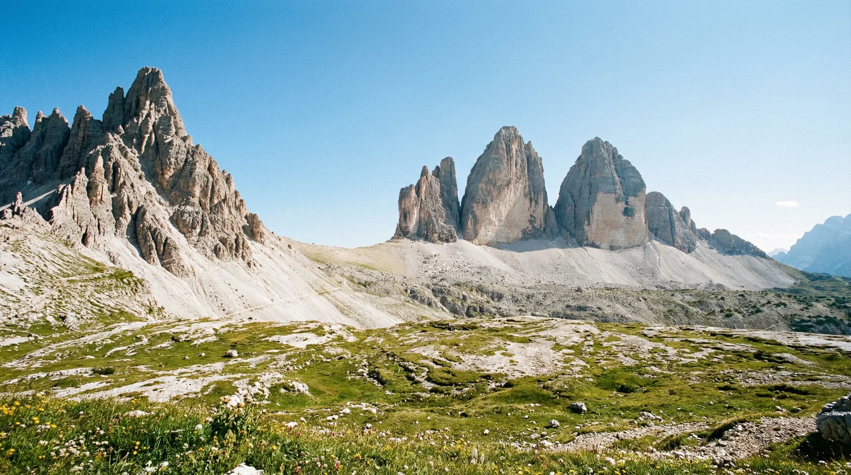 A wide shot of the three massive limestone peaks of Tre Cime di Lavaredo under a clear blue sky in the Italian Dolomites.