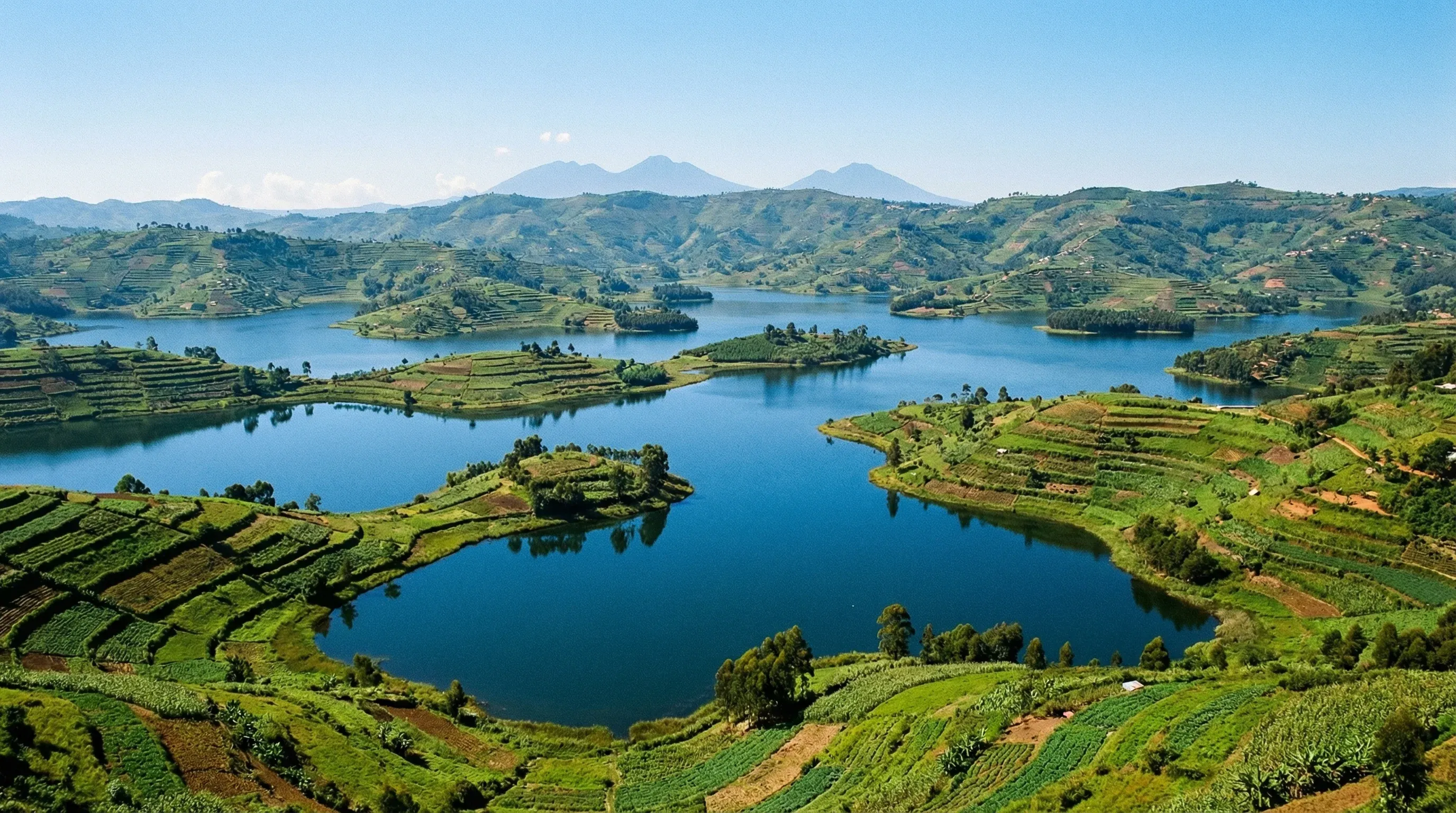 A high-angle view of Lake Bunyonyi in Uganda, showing multiple green islands in the water with volcanic mountains in the distance.