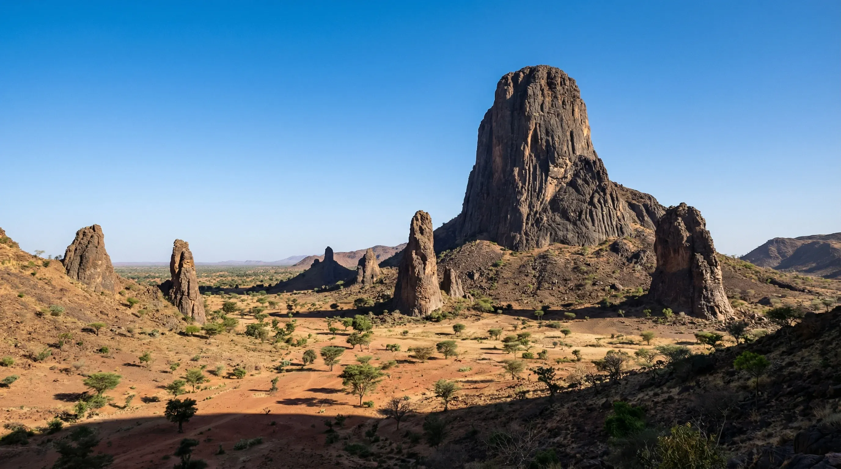 The tall, volcanic Rhumsiki Peak rising from the rocky landscape of the Mandara Mountains under a blue sky.